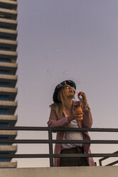 Young woman in the city blowing soap bubbles in the evening - UUF12241