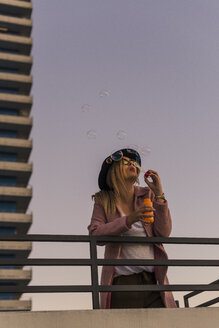 Junge Frau in der Stadt beim Blasen von Seifenblasen am Abend - UUF12241