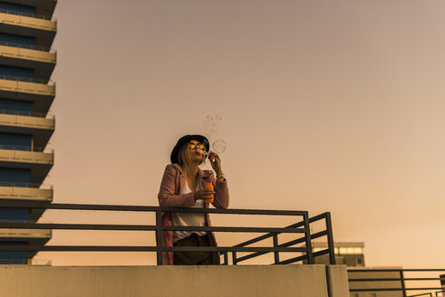 Junge Frau in der Stadt beim Blasen von Seifenblasen am Abend - UUF12242
