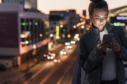 Junge Frau in der Stadt, die am Abend ihr Handy überprüft - UUF12243