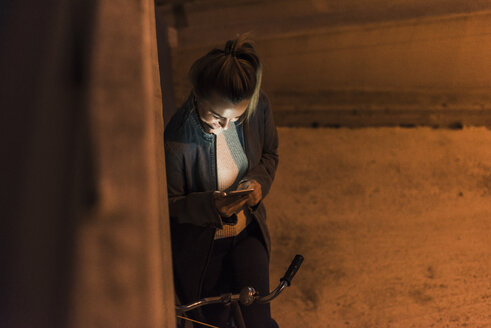 Junge Frau in der Stadt, die nachts ihr Mobiltelefon überprüft - UUF12246