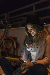 Lächelnde junge Frau in der Stadt bei der Nutzung eines Tablets in der Nacht - UUF12252