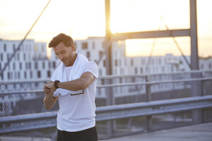 Sportler in der Stadt mit Blick auf die Smartwatch - PNEF00299