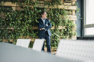 Businessman in green office looking out of window - JOSF01813