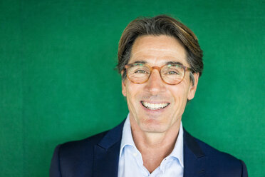 Porträt eines lächelnden Geschäftsmannes mit Brille vor einer grünen Wand - JOSF01823