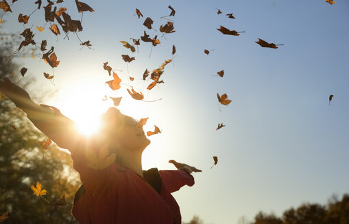 Woman throwing up autumn leaves at backlight - FCF01301