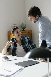 Two happy businessmen with laptop at desk in office discussing - BMF00854