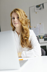 Portrait of smiling young woman with laptop at desk in office - BMF00861