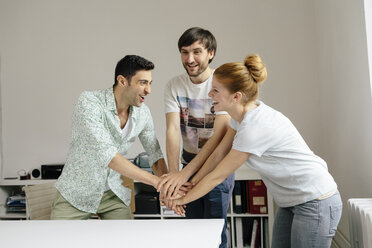 Happy colleagues in office stacking hands - BMF00880