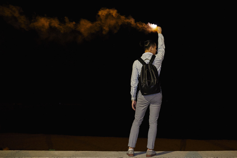 Rückenansicht eines Mannes mit Rucksack und Flamme bei Nacht, lizenzfreies Stockfoto