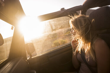 Blond woman with blowing hair sitting in car enjoying sunset - SIPF01857