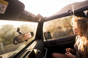 Blonde Frau mit wehenden Haaren sitzt bei Sonnenuntergang im Auto - SIPF01858