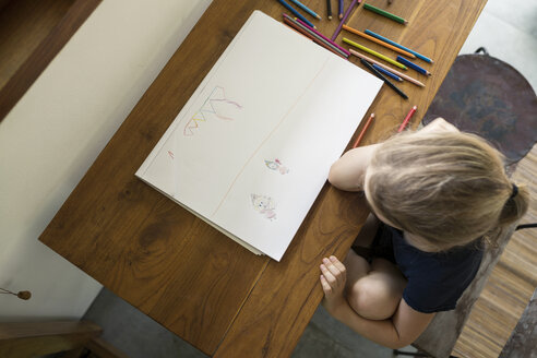 Kleines Mädchen sitzt am Tisch und zeichnet mit Buntstiften - SBOF00854