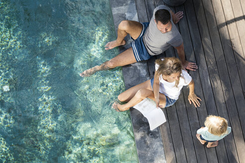 Familie sitzt am Swimmingpool, die Mutter liest ein Buch für die Kinder - SBOF00861