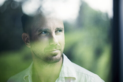 Attractive man looking through window pane, smiling, portrait - SBOF00866