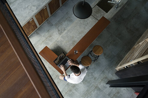 Mature man sittiing in kitchen, using laptop - SBOF00867