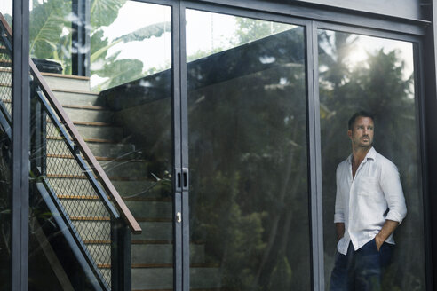 Mature man standing in his modern house, looking through window - SBOF00868