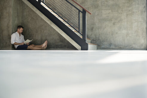 Mature man sitting under staircase, reading a book - SBOF00871