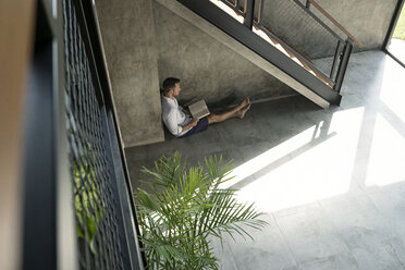 Älterer Mann sitzt unter einer Treppe und liest ein Buch - SBOF00873