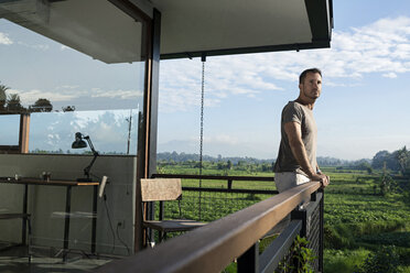 Man standing on balcony of modern house, looking at landscape - SBOF00877
