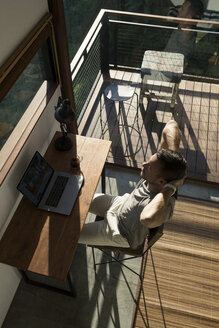 Man leaning back and taking a break from working at laptop on desk in house - SBOF00880