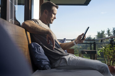 Mann sitzt auf dem Balkon eines modernen Hauses und schaut auf sein Smartphone - SBOF00882