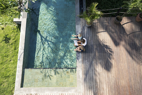 Familie sitzt am Swimmingpool, die Mutter liest ein Buch für die Kinder - SBOF00896