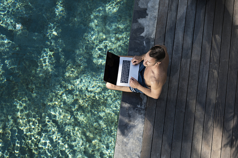 Mature man sitting at the poolside, using laptop stock photo