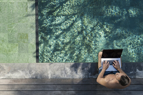 Mature man sitting at the poolside, using laptop - SBOF00898