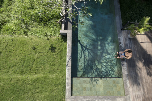 Mature man sitting at the poolside, using laptop - SBOF00899