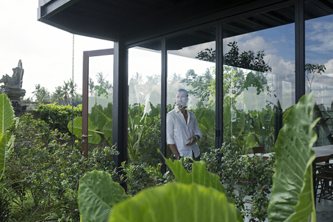 Älterer Mann steht in seinem modernen Haus und schaut durch ein Fenster, lizenzfreies Stockfoto