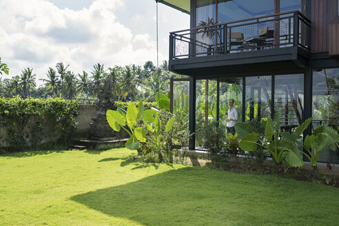 Mature man standing in his modern house, looking through window - SBOF00913