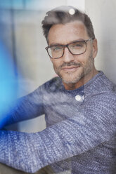 Porträt eines lächelnden Mannes hinter einer Glasscheibe mit Brille - PNEF00325