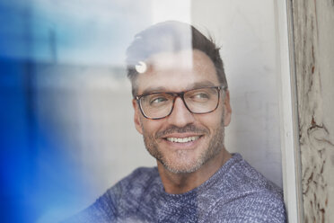 Portrait of smiling man behind glass pane wearing glasses - PNEF00327