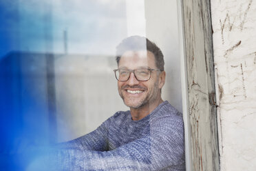 Portrait of laughing man behind glass pane wearing glasses - PNEF00328
