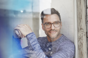 Portrait of man wearing glasses behind glass pane - PNEF00329