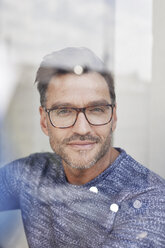 Porträt eines lächelnden Mannes hinter einer Glasscheibe mit Brille - PNEF00330
