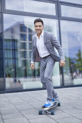 Portrait of smiling businessman skateboarding on pavement - PNEF00332