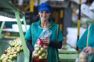 Porträt einer lächelnden Frau mit Äpfeln in Plastiktüten in einer Fabrik - ZEF14713
