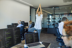 Frau übt Yoga im Büro, umgeben von beschäftigten Kollegen - ZEDF00972
