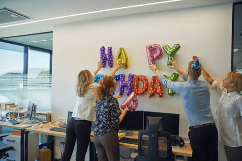 Colleagues decorating office with happy birthday writing - ZEDF00974