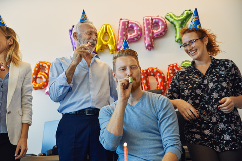 Kollegen feiern Geburtstag im Büro mit Partybläsern und Partyhüten, lizenzfreies Stockfoto