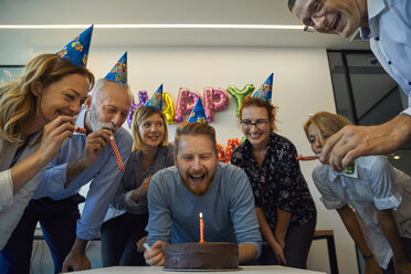 Colleagues having a birthday celebration in office with cake, party blower and party hats - ZEDF00976