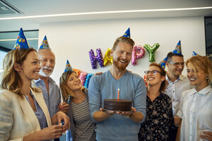 Kollegen feiern Geburtstag im Büro mit Kuchen und Partyhüten - ZEDF00977