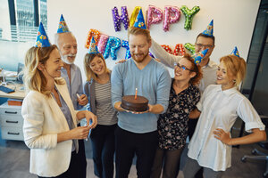 Kollegen feiern Geburtstag im Büro mit Kuchen und Partyhüten - ZEDF00978