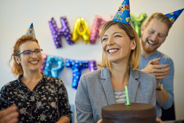 Colleagues having a birthday celebration in office with cake and party hats - ZEDF00982