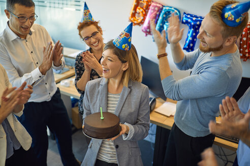 Colleagues having a birthday celebration in office with cake and party hats - ZEDF00983