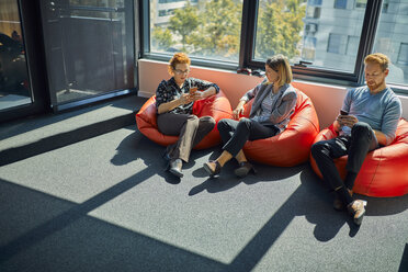 Colleagues with cell phones sitting in bean bags in office lounge stock  photo