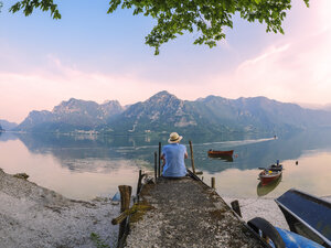 Italy, Lombardy, back view of man sitting on jetty at Lake Idro at morning twilight - LAF01948