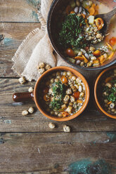 Mediterrane Suppe in Kupfertopf und Terrakottaschalen auf Holz - GIOF03296